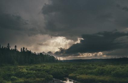 Photo d'une mare dans une prairie sous un ciel orageux