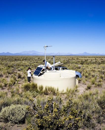 Photo de deux chercheurs installant une antenne sur une cuve de l'observatoire Pierre Auger dans la pampa Argentine