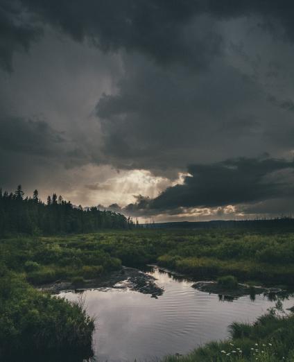 Photo d'une mare dans une prairie sous un ciel orageux