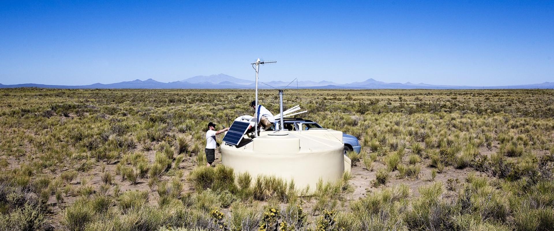 Photo de deux chercheurs installant une antenne sur une cuve de l'observatoire Pierre Auger dans la pampa argentine