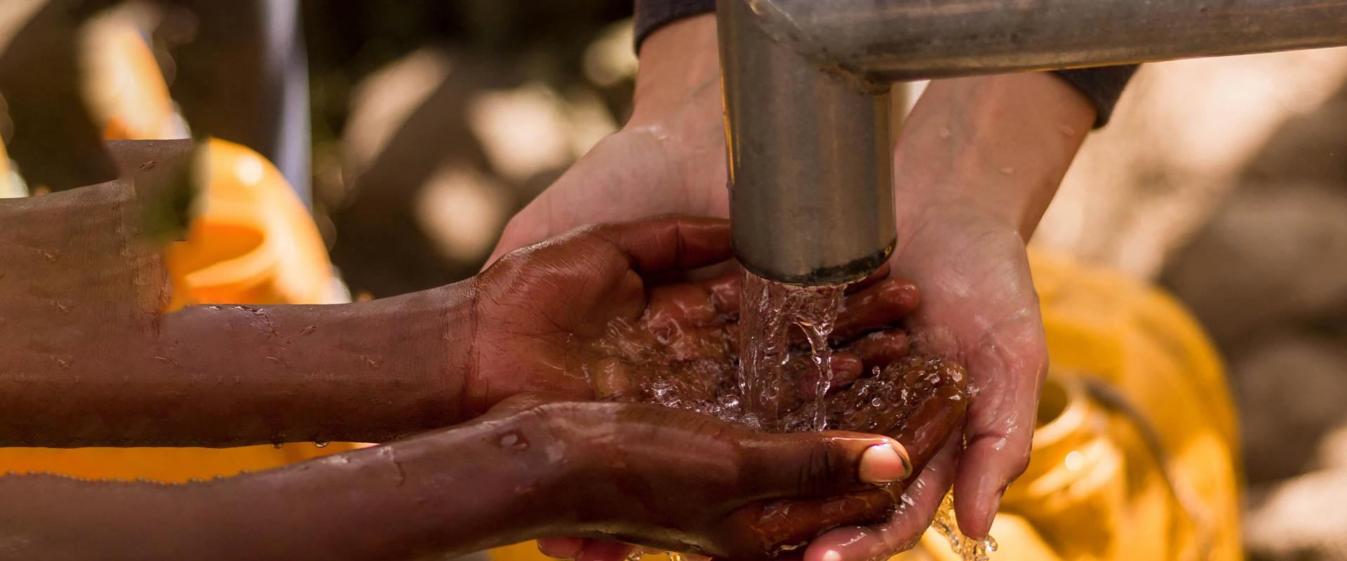 Photo de deux paires de main recueillant de l'eau sous un robinet