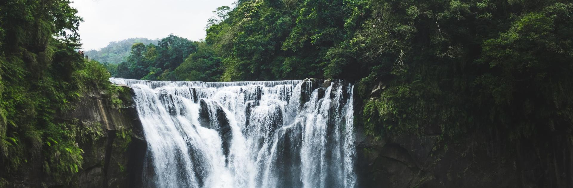 Photo d'une cascade se déversant dans un bassin et entourée d'arbres verts